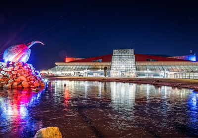 KEF airport exterior shot, showing a modern glass terminal building lit up by colourful lights and LED's at night