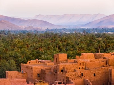 A view of a desert village in Morocco, with palm trees and mountains in the background